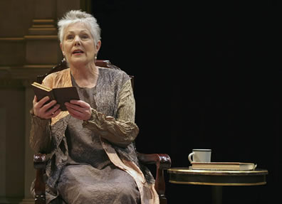 Lynn Redgrave reading from a book next to a table